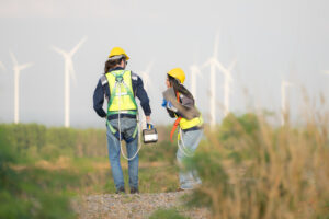 Engineer and worker discussing on a wind turbine farm with laptop